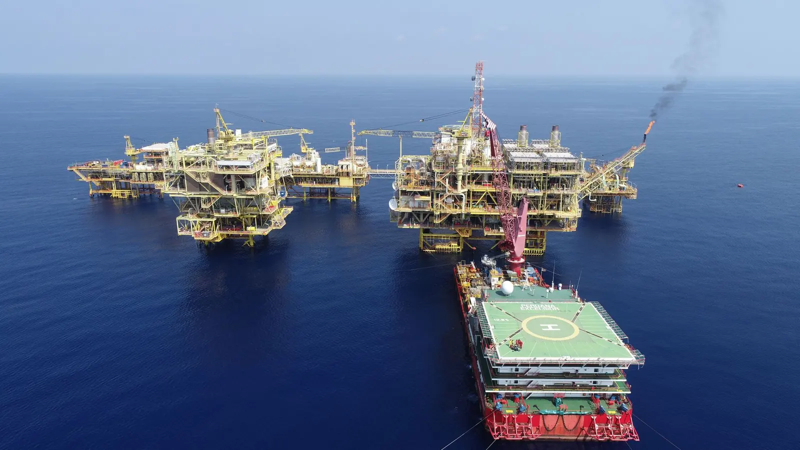 Aerial view of a group of linked offshore platforms with a support vessel alongside