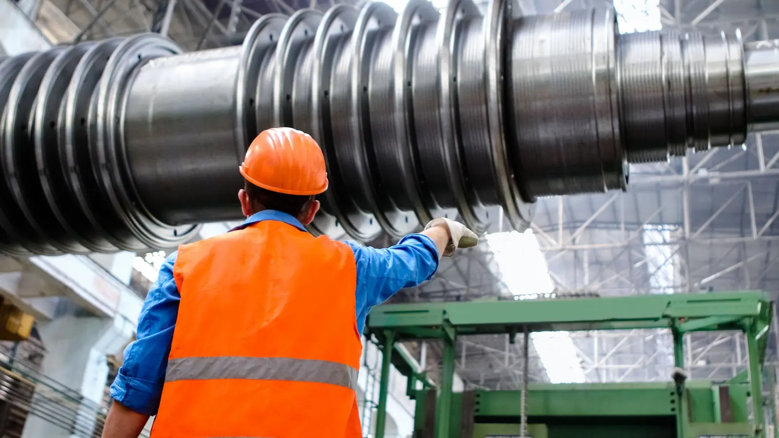 A technician in a hard hat and high-visibility vest inspecting a large steel rotor