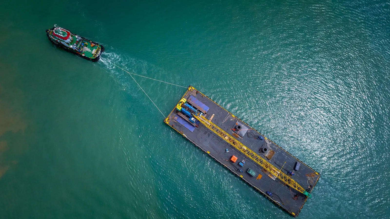 A tug towing a loaded barge across open water, seen from above